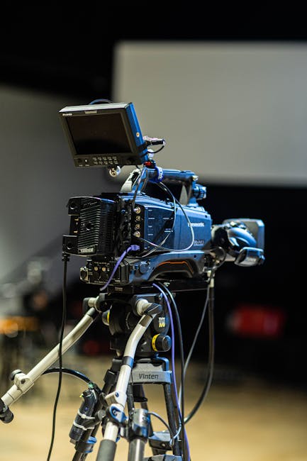 Modern video camera with liquid crystal display and connected cables on stage in building
